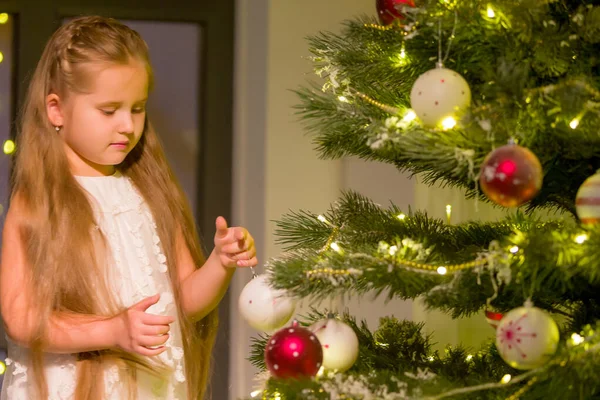 Klein meisje versiert een kerstboom. Nieuwjaarsconcept, gezinsvakanties. — Stockfoto