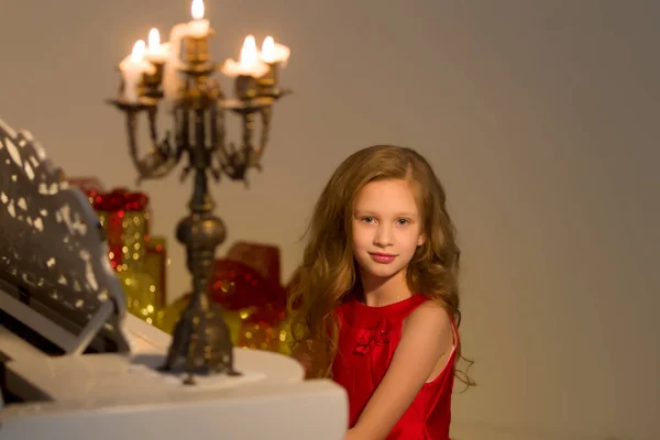 一个漂亮的女孩坐在一架古典钢琴上，上面点着燃烧的蜡烛. — 图库照片