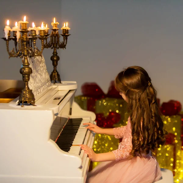 美丽的女孩弹钢琴，看着燃烧的蜡烛 — 图库照片