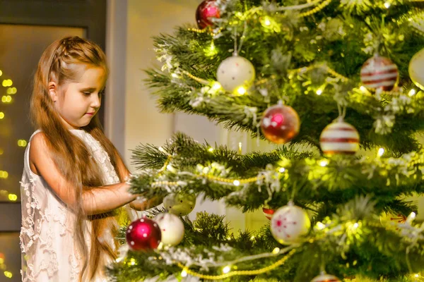 Küçük kız bir Noel ağacını süslüyor. Yeni yıl konsepti, aile tatilleri. — Stok fotoğraf