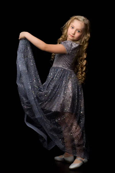 En liten flicka i en lång, elegant klänning av en prinsessa på en svart bakgrund. — Stockfoto