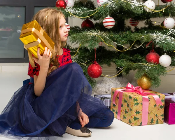 Mooi meisje zitten op de vloer in de voorkant van de kerstboom met Geschenkdoos. — Stockfoto