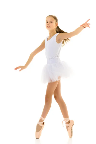 Schattig klein meisje in een tutu en pointe schoenen dansen in de studio op een witte achtergrond. — Stockfoto