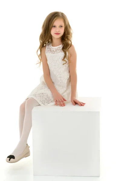 Menina loira bonita em vestido branco sentado no cubo em seu joelho — Fotografia de Stock
