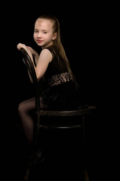 Porträt eines kleinen Mädchens auf einem alten Wiener Stuhl, schwarzer Hintergrund. — Stockfoto