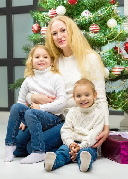 Χαρούμενη μαμά και χαριτωμένο κόρη και ο γιος της κάθεται επόμενο χριστουγεννιάτικο δέντρο. — Φωτογραφία Αρχείου