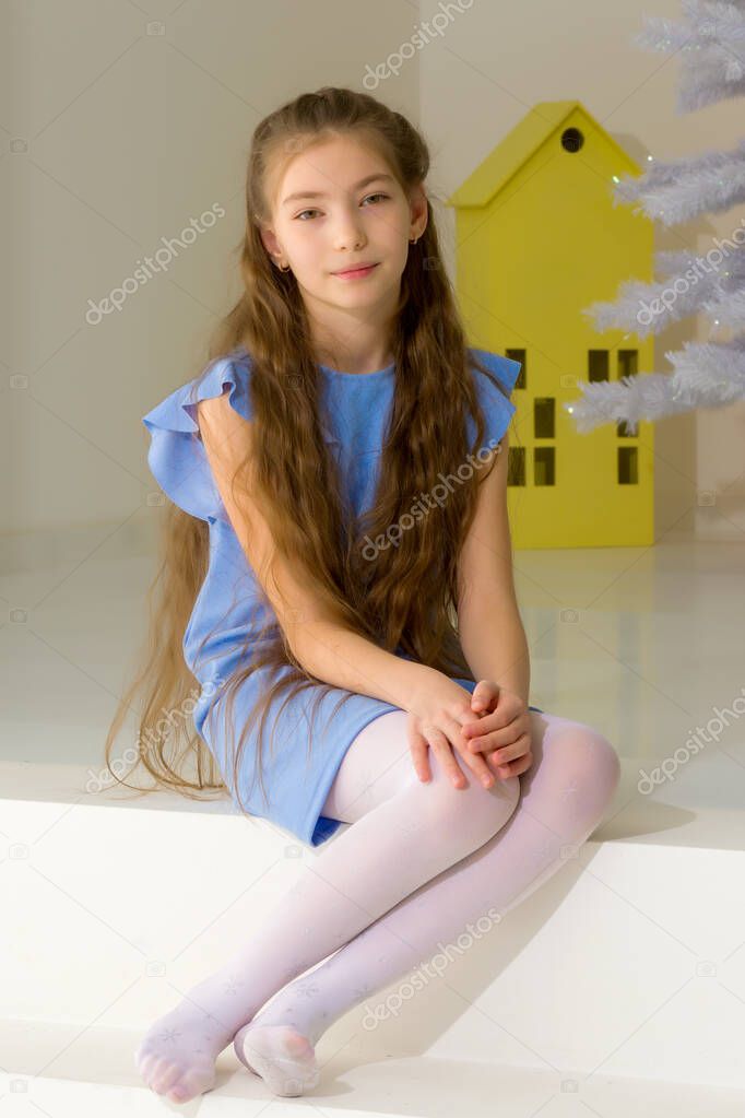 Girl in Stylish Dress Sitting on the Floor in Front of Christmas Tree.