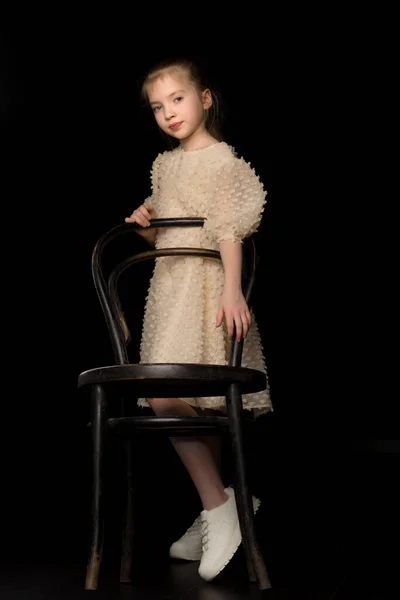 Portrait d'une fille debout sur un fond noir près de la vieille chaise viennoise. — Photo