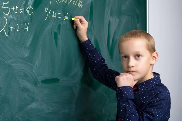 Skolpojke skriver på tavlan i klassrummet — Stockfoto