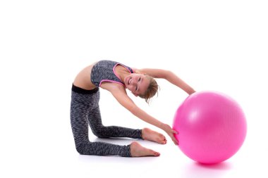 Küçük kız spor yapmak için büyük bir top üzerinde egzersiz yapıyor..