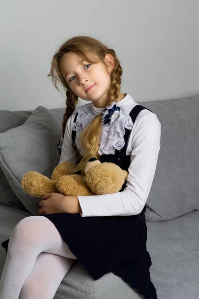 Милая школьница, сидящая на диване с плюшевым мишкой — стоковое фото