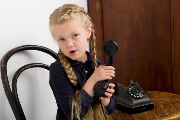 Flicka sitter på stol och pratar med gamla telefonen — Stockfoto