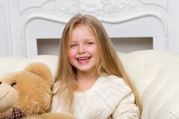 Kanepede oturan ve oyuncak ayıyı kucaklayan kız.