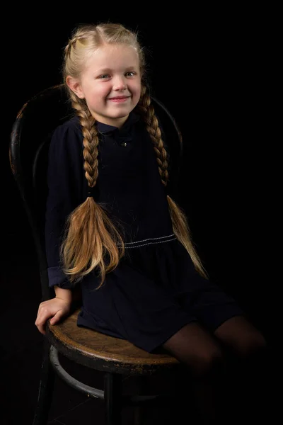 Blond meisje zitten op stoel in donkere kamer — Stockfoto