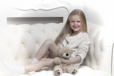 Kanepede oturan ve oyuncak ayıyı kucaklayan kız.