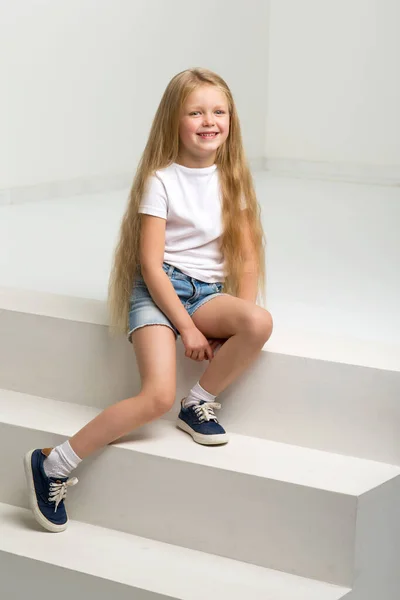 Κορίτσι σε casual ρούχα κάθεται σε λευκή σκάλα — Φωτογραφία Αρχείου