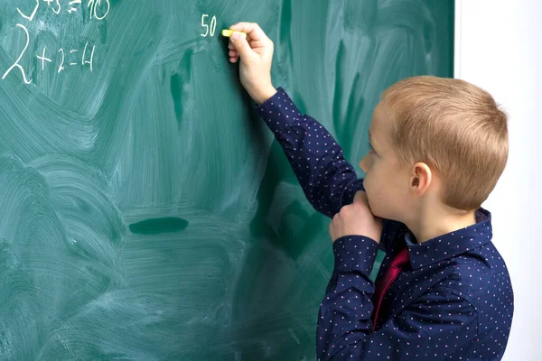 Skolpojke skriver på tavlan i klassrummet — Stockfoto