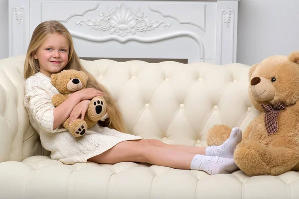 Menina sentada no sofá abraçando ursinho de pelúcia — Fotografia de Stock