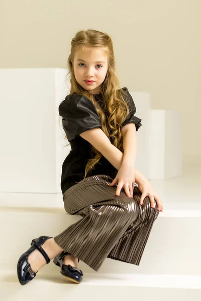 Petite fille pose pour un magazine en studio sur un cube blanc. — Photo