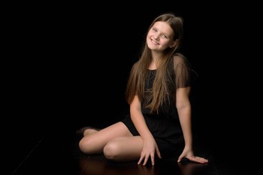 Gülümseyen kız yerde oturmuş dizlerine sarılıyor.