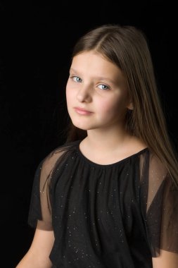 Siyah arka planda poz veren sevimli, gülümseyen küçük bir kızın yakın görüntüsü.