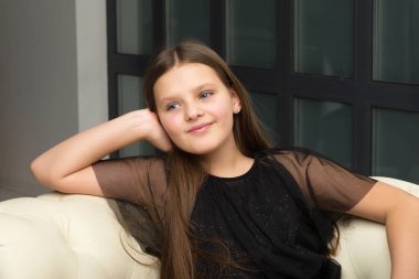 Kanepede oturan sevimli gülümseyen kız. Stüdyoda fotoğraf çekimi.