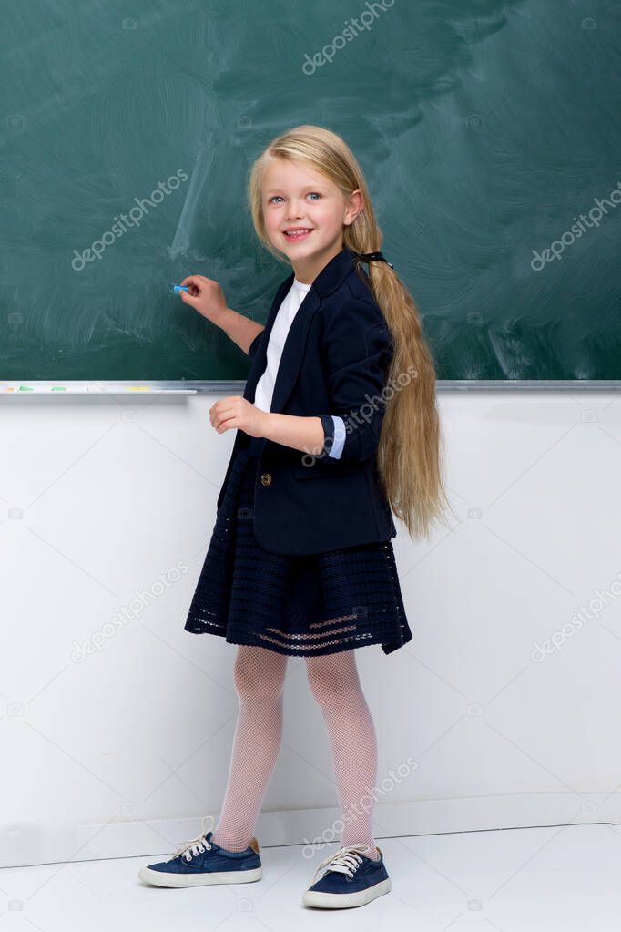 Beautiful schoolgirl standing at blackboard. Photo session in the studio