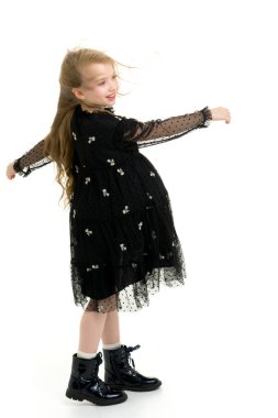 Güzel küçük bir kız rüzgârda duruyor, saçları ve kıyafetleriyle..