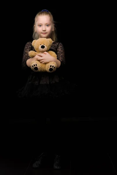 Маленькая девочка с плюшевым мишкой на черном фоне. — стоковое фото
