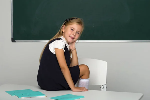 Liebenswertes Schulmädchen sitzt auf Schreibtisch im Klassenzimmer — Stockfoto