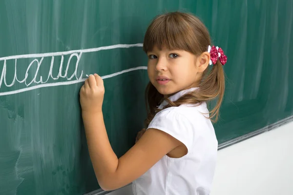 Allvarlig skolflicka stående vid svarta tavlan — Stockfoto