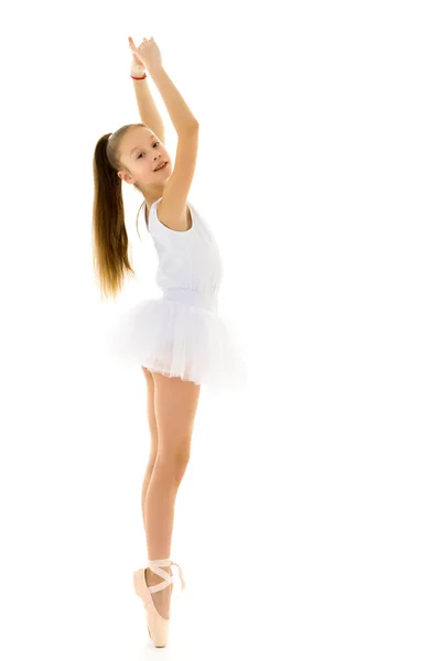 Schattig klein meisje in een tutu en pointe schoenen dansen in de studio op een witte achtergrond. — Stockfoto