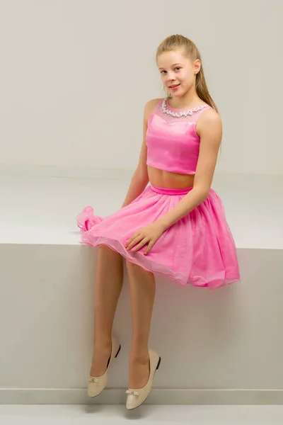 Krásná dívka na sobě růžová nádrž top a sukně sedí na okraji — Stock fotografie