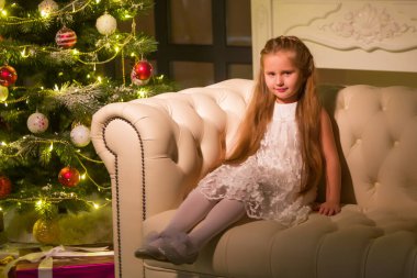 Yeni yıl ağacının yanındaki kanepede oturan güzel küçük kız..