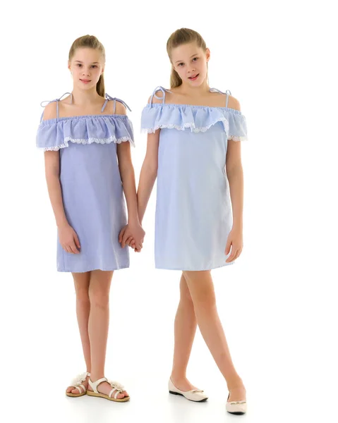 Сестры в одинаковых легких платьях стоят и держатся за руки — стоковое фото
