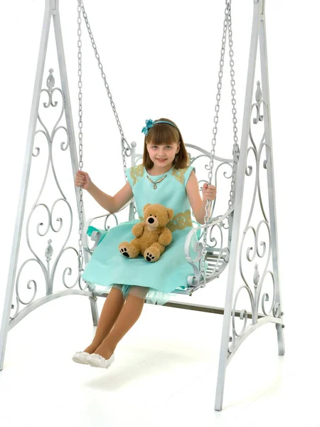 Uma menina está balançando em um balanço com um urso de pelúcia. — Fotografia de Stock