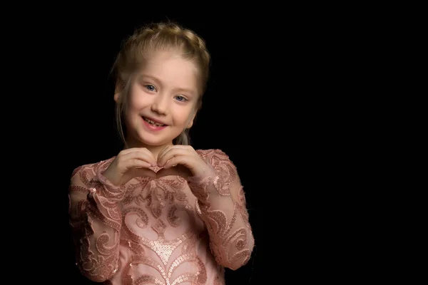 Niña hace un corazón con sus manos y sonríe sobre un fondo negro. — Foto de Stock