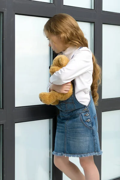 一个小女孩站在窗边抱着一只泰迪熊. — 图库照片