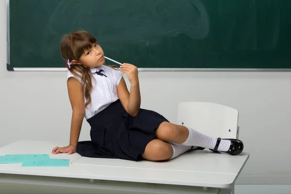 Cute girl sitting on desk in classroom — Stock Photo, Image