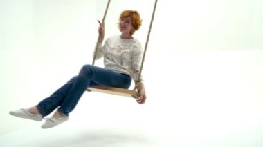 Beyaz stüdyo geçmişine karşı salıncakta sallanan güzel genç bir kadın