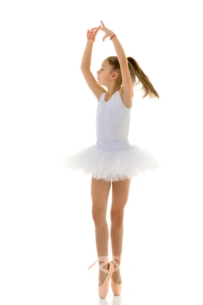 Schattig klein meisje in een tutu en pointe schoenen dansen in de studio op een witte achtergrond. — Stockfoto