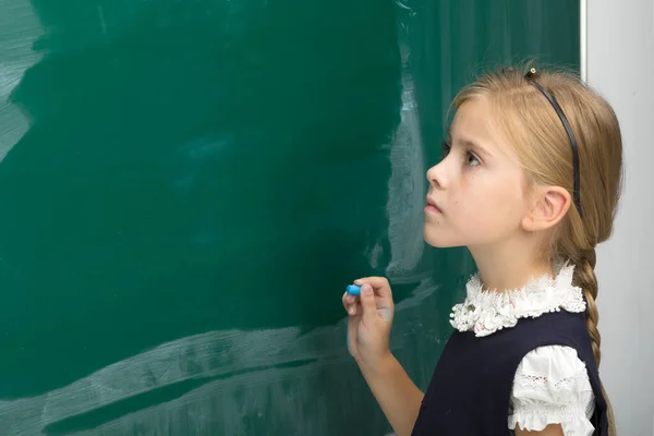 Liebenswertes Schulmädchen schreibt auf grüne Kreidetafel — Stockfoto