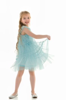 Küçük bir kız ellerini eteğin kenarlarında tutuyor..