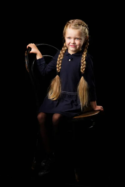 Blond meisje zitten op stoel in donkere kamer — Stockfoto