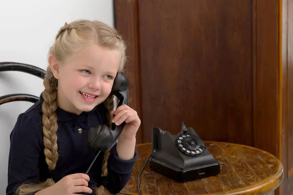 Flicka sitter på stol och pratar med gamla telefonen — Stockfoto