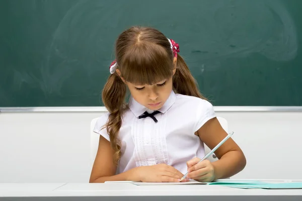 Iskoláslány ül az íróasztalnál és jegyzetfüzetbe ír. — Stock Fotó