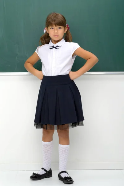 Söt flicka i skoluniform stående vid svarta tavlan — Stockfoto