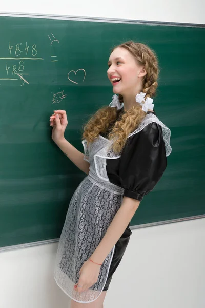 Menina da escola feliz em uniforme escrevendo no quadro negro — Fotografia de Stock