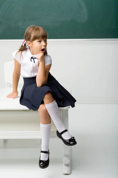 Glad skolflicka sitter på skrivbordet i klassrummet — Stockfoto