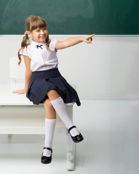 Happy school girl sitting on desk in classroom